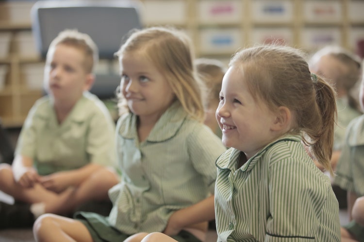 Two students smiling at their teacher as they enjoy listening to a story she is reading.