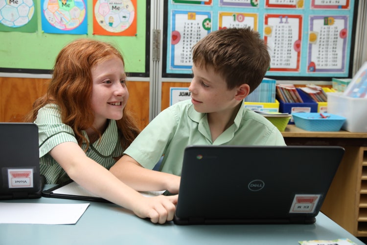 Two students collaborating and assisting each other on a laptop during a STEM lesson.