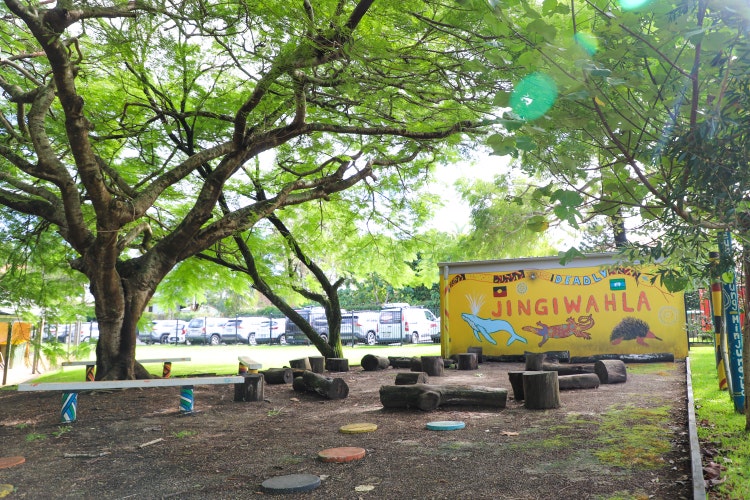 A photograph of our school cultural space. It is surrounded by beautiful trees and a mural. There is a circle of logs that are used as seats and colourful stepping stones that lead you to the circle.