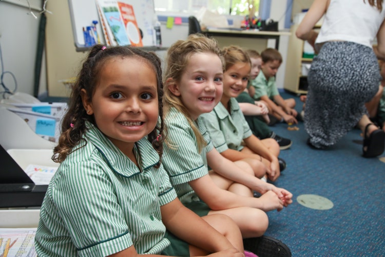 A group of students sitting in a circle, smiling at the camera, and ready to take part in a learning activity, proudly showing their sense of belonging at Banora Point Public School.