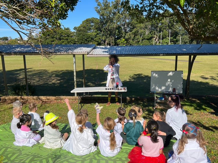 A teacher guiding a group of students dressed as scientists through a science experiment.