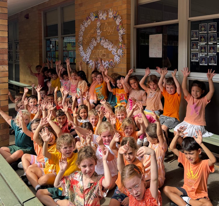 Kindergarten students raising their hands in front of their Harmony Day display.