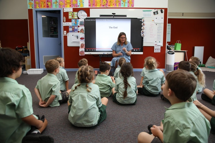 A Kindergarten teacher asking guiding questions to the class after listening to a text with students seated on the floor.