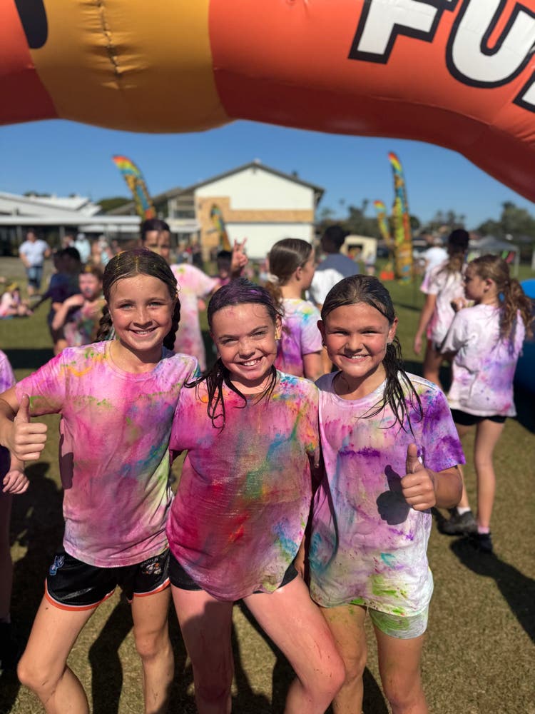 Students covered in vibrant colours, smiling happily as they take part in the Colour Fun Run.