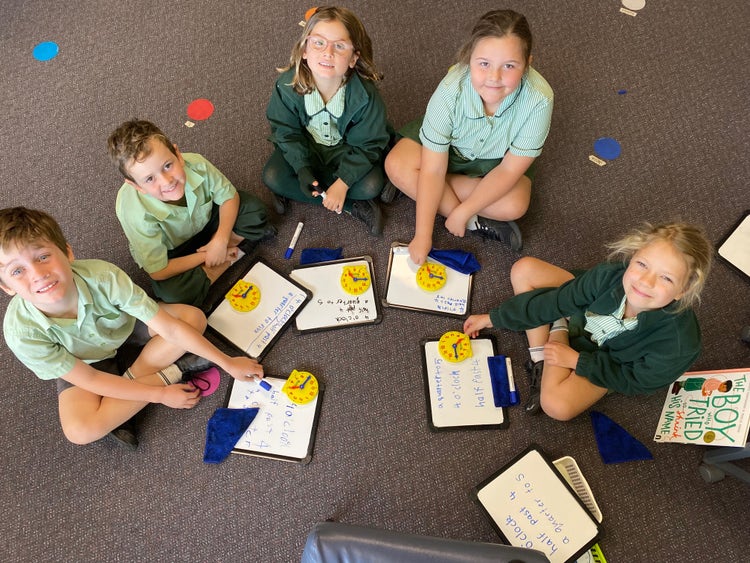 A small maths group focused on helping students understand analogue clocks. Students are setting the time on the clocks and matching it to the written words on a whiteboard.