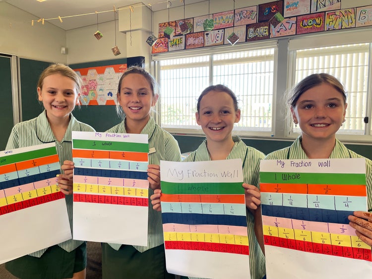 Students holding their fraction walls made from coloured paper, with each strip folded equally and labelled to show different fractions.