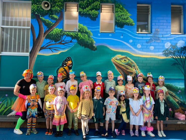 Kindergarten students smiling at the camera after celebrating 100 days at school, each wearing a crown they designed for the occasion and dressed in bright clothes to show they are