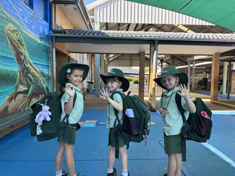 Students waving goodbye at the end of the school day with their school hats on and school bags on their back.