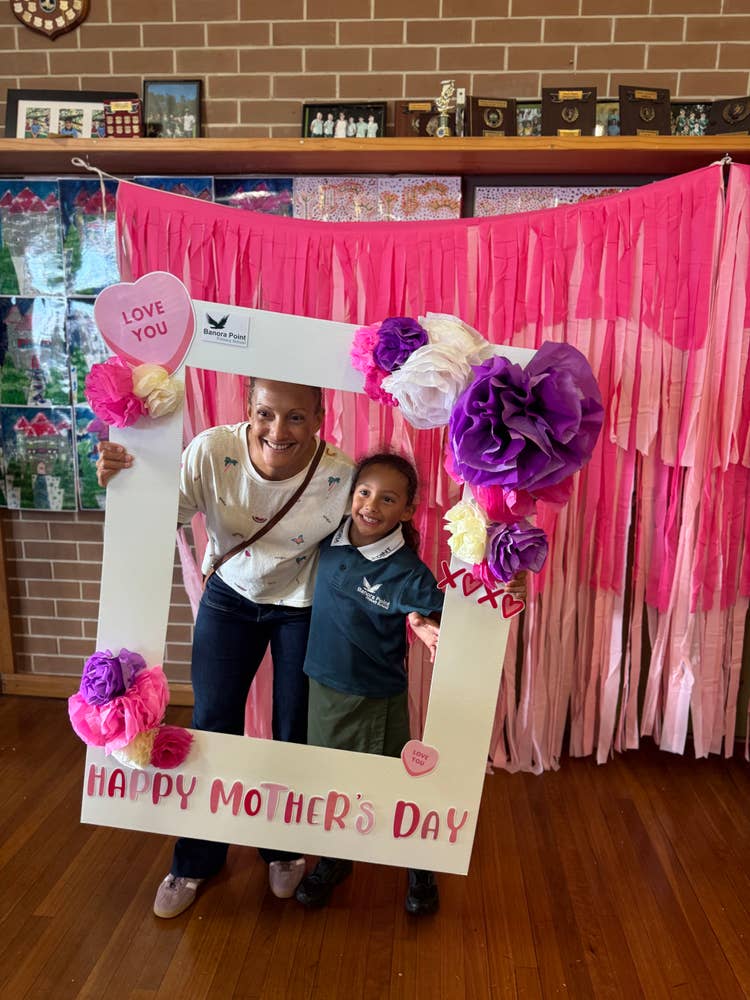 A young student and mother holding an enlarged photo frame smiling happily together.