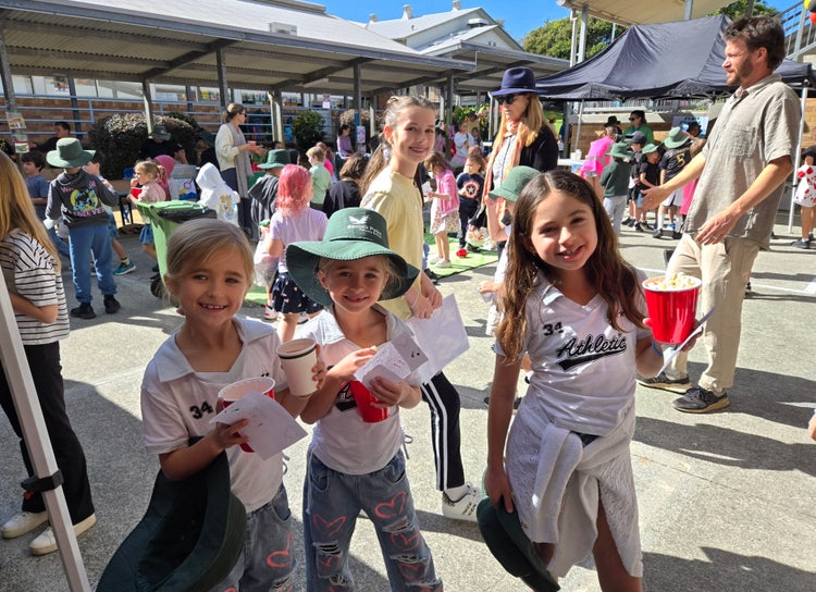 Three students holding popcorn cups and smiling happily at the camera.