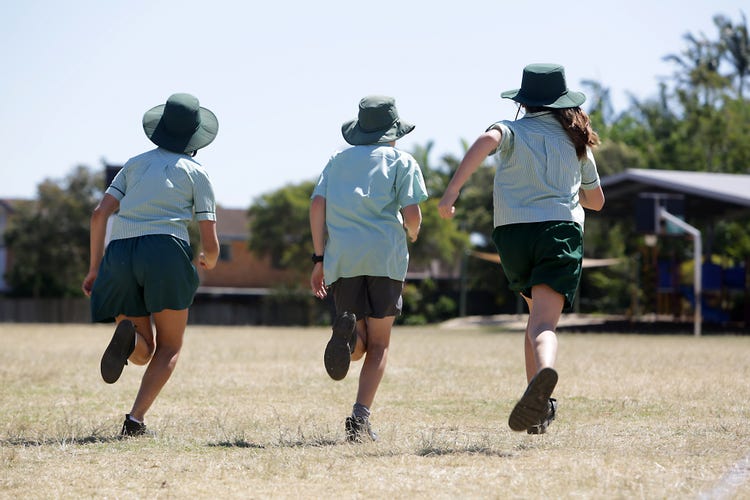 Three students running away from the camera on the school oval. They are dressed in their day school uniform with a hat on their head.