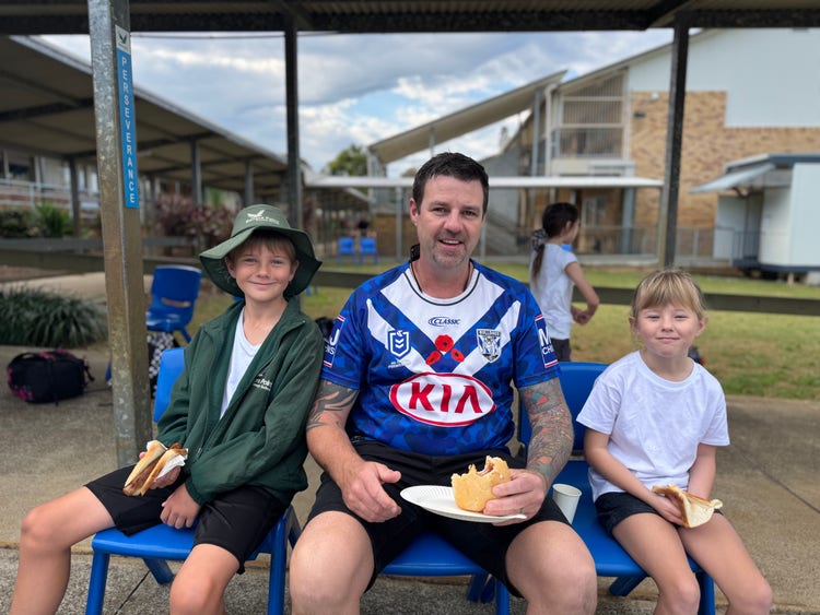 A father and his two children sitting whilst enjoying a BBQ breakfast.