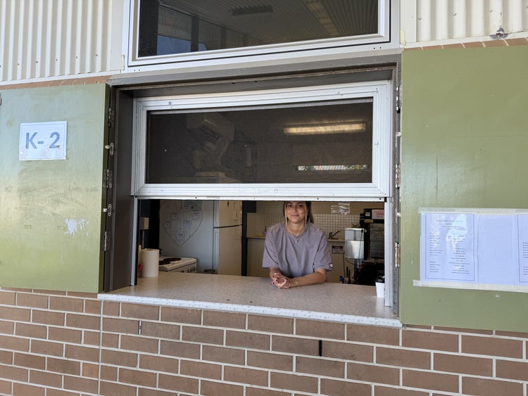 One of our helpers in the canteen standing behind the window with a smile on her face. The canteen menu is displayed on the left.